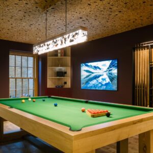 A luxury games room with a custom pool table, a large wall mounted TV and custom cue & ball wall mounted cabinetry.