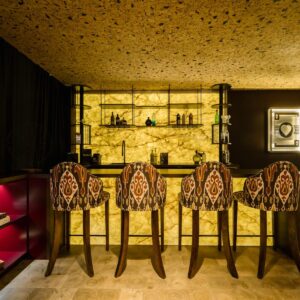 A luxury games room with cork ceiling, natural wooden flooring and a custom back lit stone wall bar with bar stools.