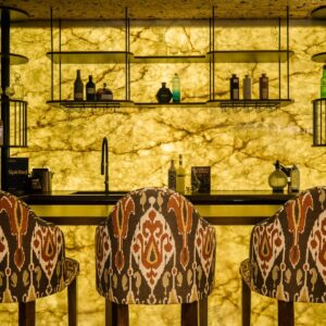 A luxury games room close up of a custom back lit stone wall bar with bar stools.