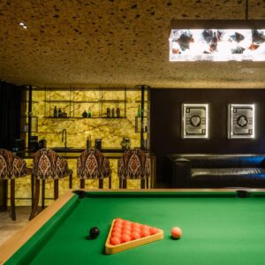 A luxury games room with cork ceiling, view across the pool table to the custom back lit stone wall bar with bar stools.