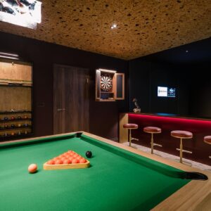 A close up view across the pool table of a custom dart board cabinet and cue and ball cabinet.