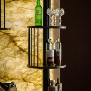 A close up view of a custom back lit stone wall bar with circular shelving with spirit bottles.