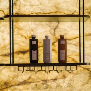 A close up view of a custom back lit stone wall bar with custom shelf with gin bottles mounted and a glass holder.