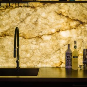 A close up view of a custom back lit stone wall bar with sink.