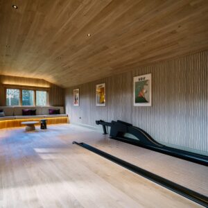 Games room with timber clad vaulted ceiling, bespoke duck pin bowling lane and ball return, and a curved built-in banquette with under-seat lighting and 3D-printed duck pin-shaped pendant lights.