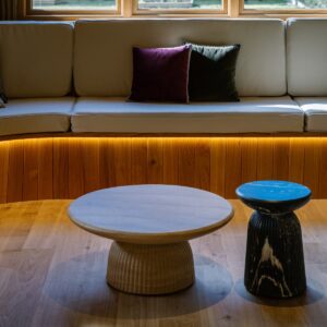 Games room curved upholstered banquette with timber clad base and warm concealed LED lighting, styled with nested round coffee tables on oak flooring.