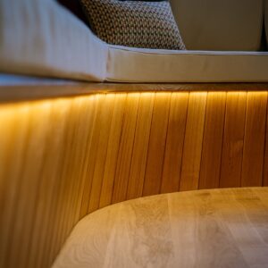 Games room close-up of the curved banquette with a timber clad base and concealed warm LED strip lighting beneath the upholstered seating.