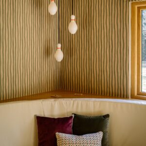 Games room corner with curved built-in banquette seating and three unlit 3D-printed duck pin-shaped pendant lights above striped walls, part of the duck pin bowling space.