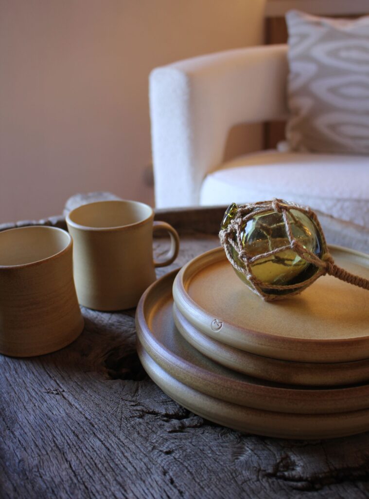 Handmade ceramics by Marc Marcet styled on a rustic timber table with cups, plates and a glass fishing float, celebrating local craft and natural materials.