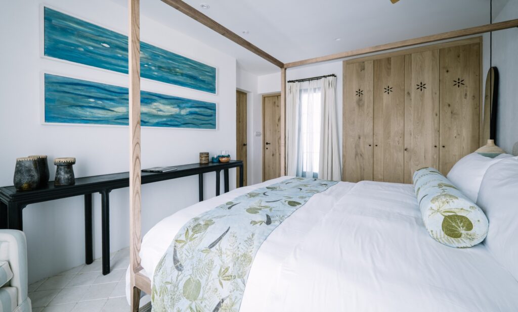 Bedroom featuring commissioned botanical textiles by Turid Ljosnes Tarabay alongside blue-toned artwork by Magda Triay, creating a calm interior shaped by Menorcan artisan craft.