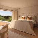 Property renovation in Menorca shown as a 3D render of a calm Menorcan villa bedroom with natural textures, patterned headboard, soft pendant lighting and views across the landscape.