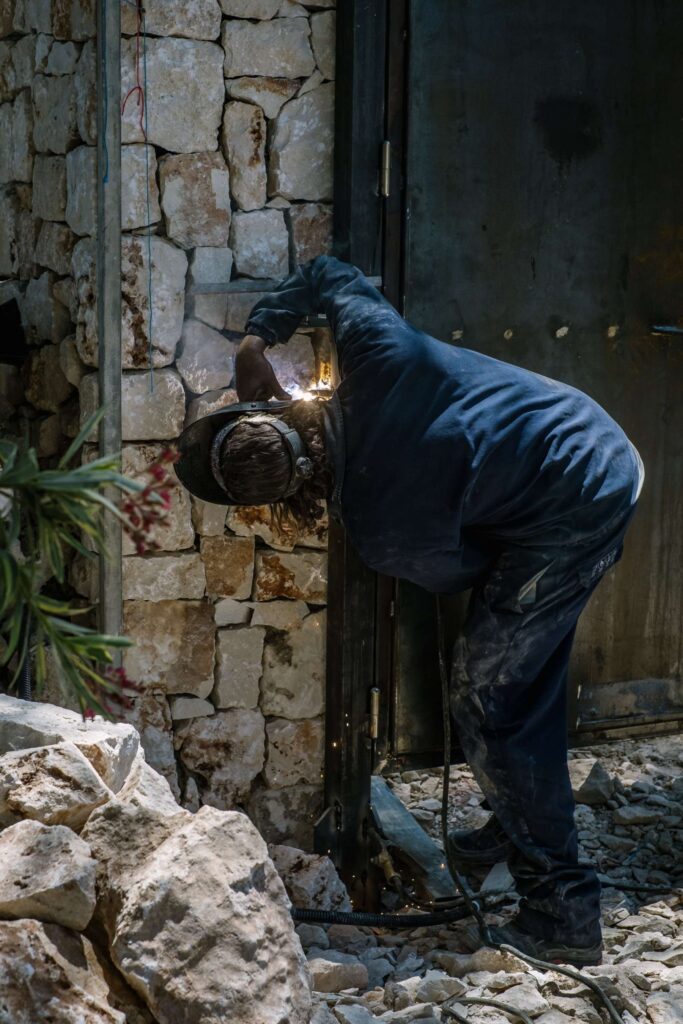 Property renovation in Menorca showing a tradesperson welding a metal gate beside a traditional stone wall during exterior renovation works.