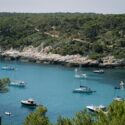 Menorca coastline with turquoise water, sailing boats, rocky cliffs and pine forest, reflecting the island landscape that shapes the design approach.